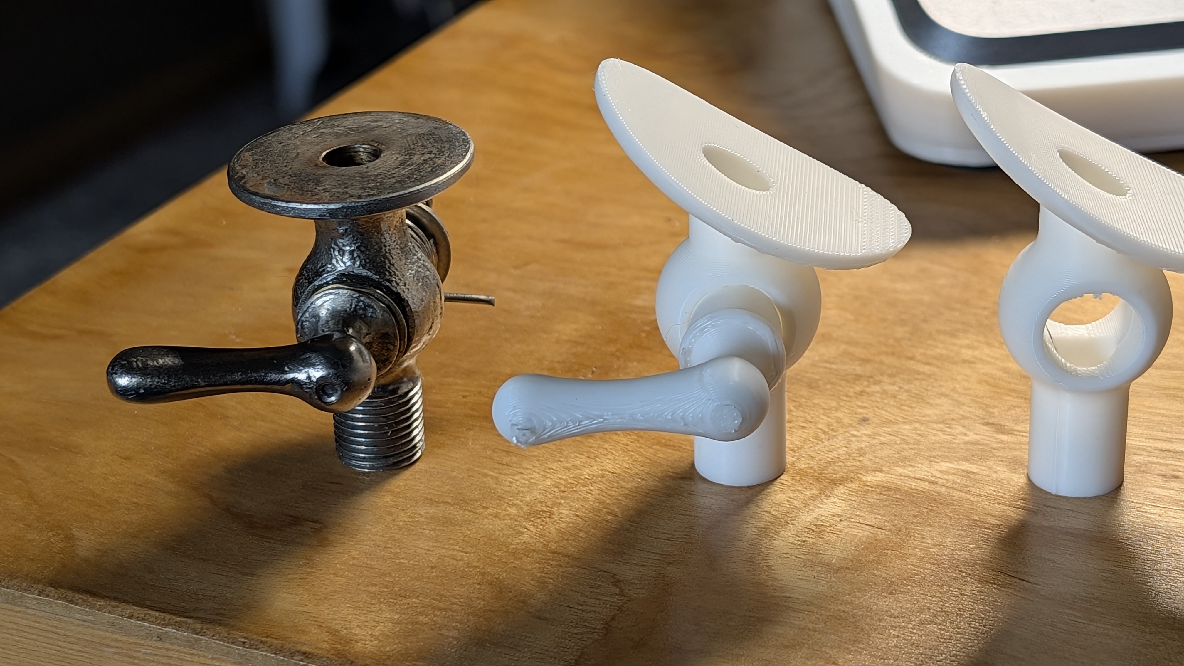 An original vintage metal component beside several white 3D-printed test versions